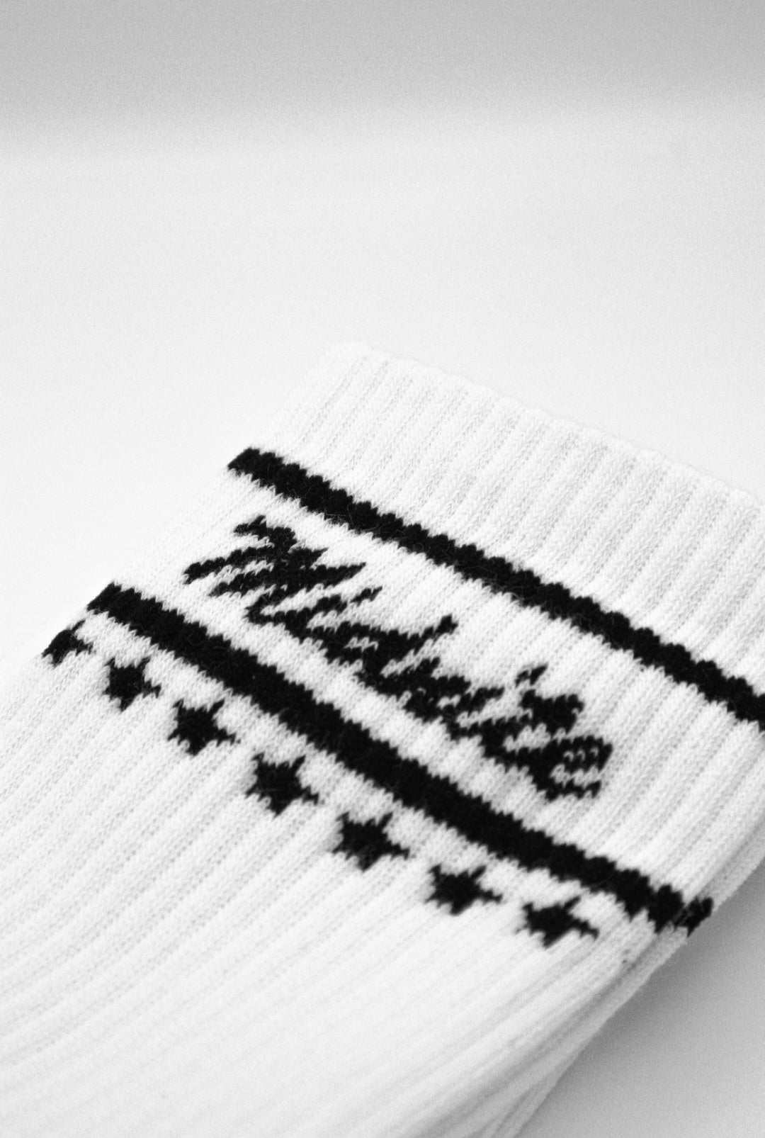 Midnite Club white streetwear socks – ribbed athletic crew socks with black cursive logo and star detailing, inspired by retro motorsport and underground fashion.